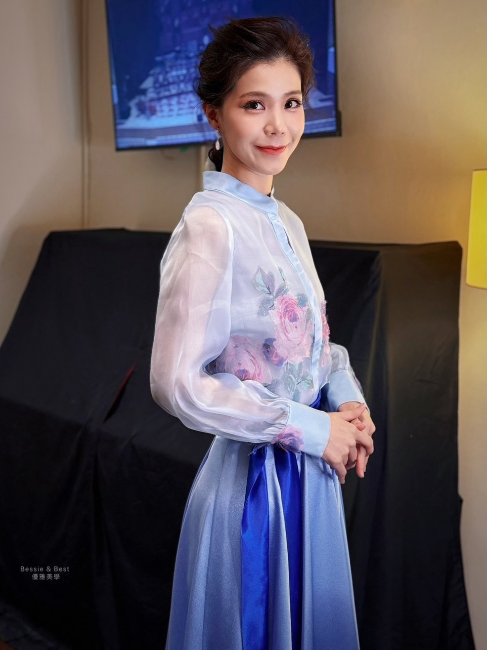 趙怡然首席後台梳化完成側拍・水藍立領花卉紗衫搭配緞面寶藍長裙，後方螢幕連線國家音樂廳舞台